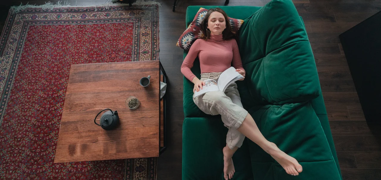 Eine Frau liegt gemütlich auf dem Sofa, neben ihr liegt auf dem Boden ein orientalischer, klassischer Teppich unter dem Tisch. - Eine Frau liegt gemütlich auf dem Sofa, neben ihr liegt auf dem Boden ein orientalischer, klassischer Teppich unter dem Tisch.