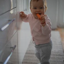 Ein Baby steht in der Küche auf einem Teppich und isst eine Möhre - Ein Baby steht in der Küche auf einem Teppich und isst eine Möhre